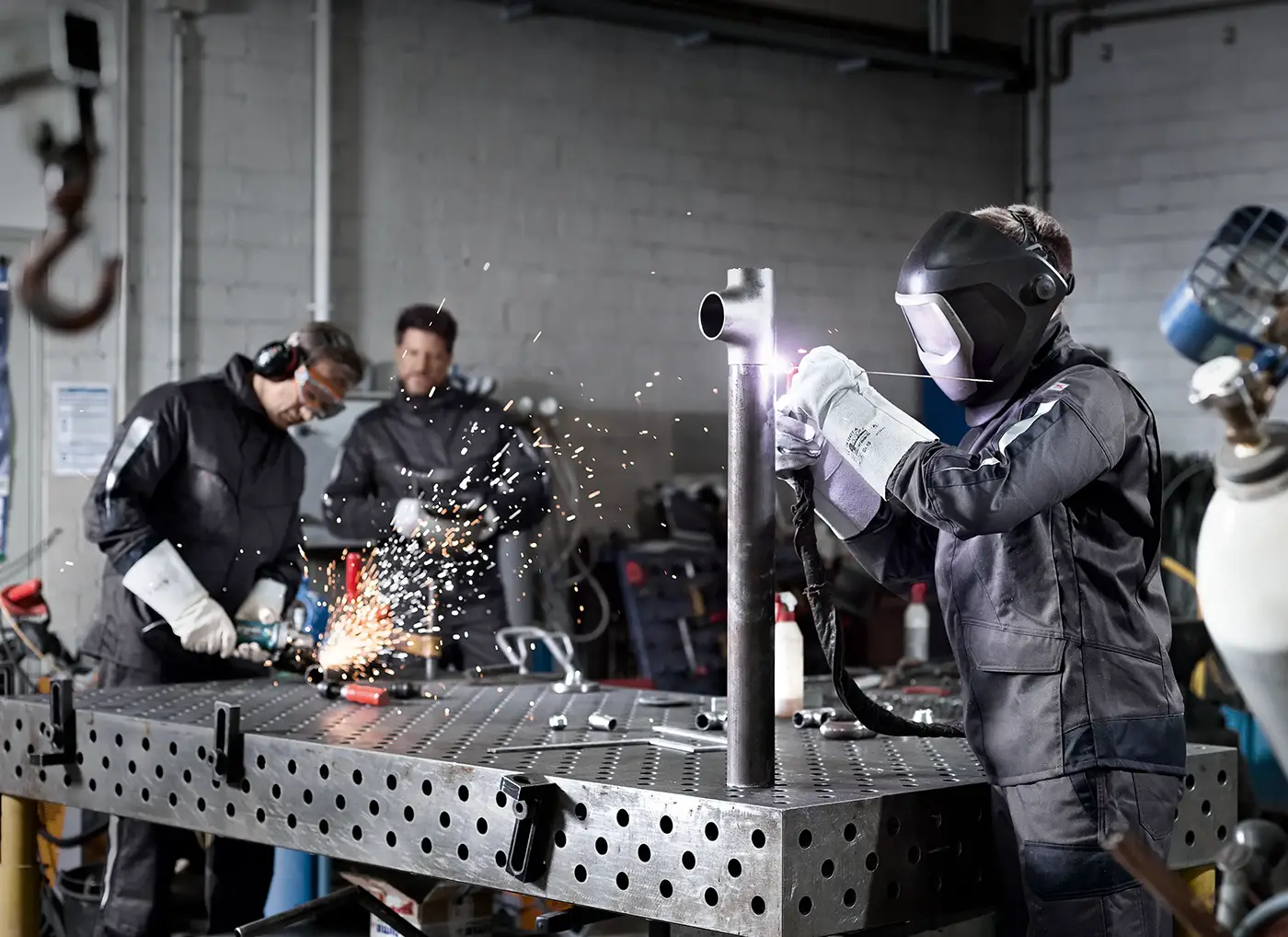 Arbeitende mit professioneller Arbeitsschutzausrüstung in einer Werkstatt bei Schweißarbeiten