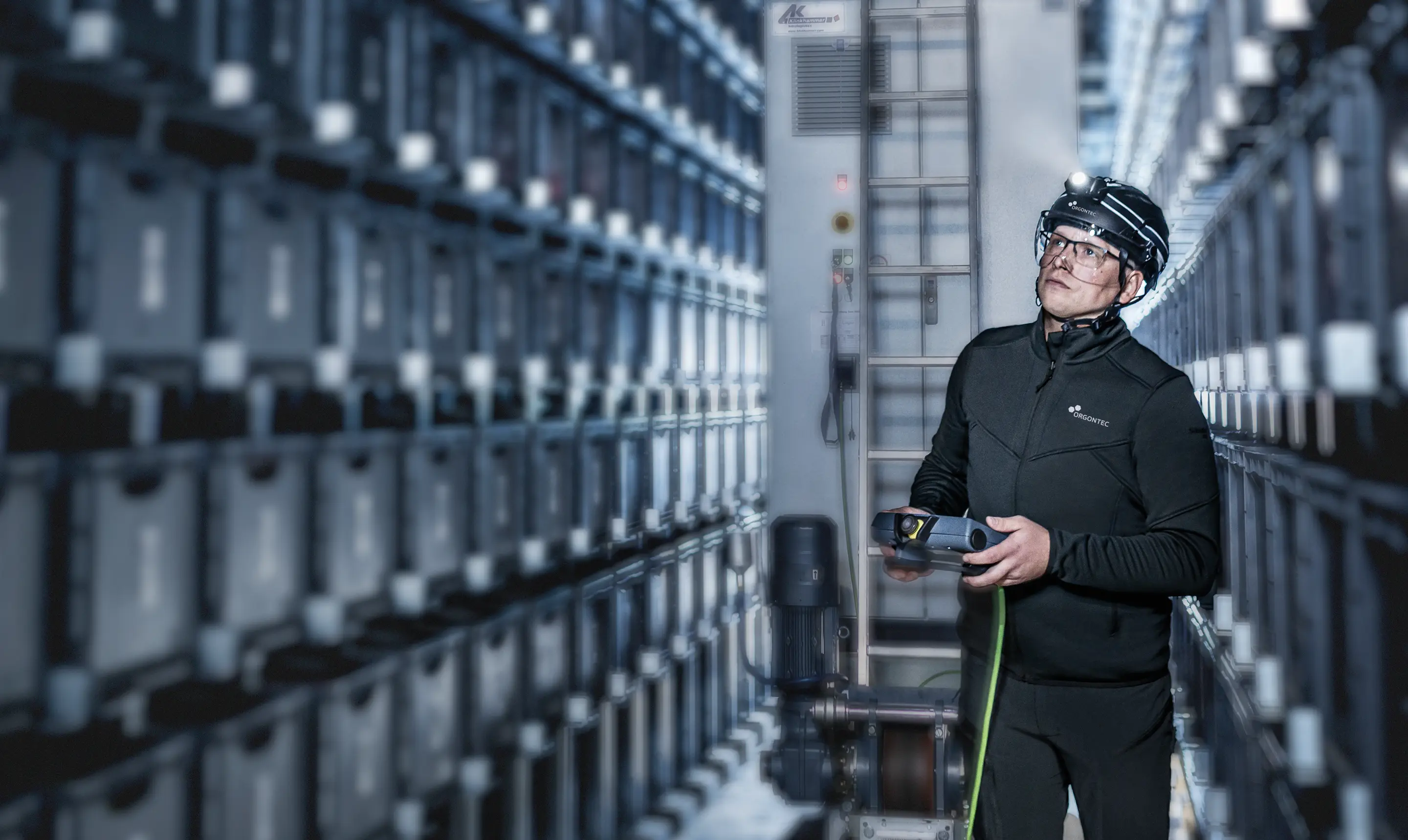 Mitarbeiter mit Coporate Teamwear, Schutzhelm und Stirnlampe zwischen den Gängen eines Hochregal-Lagers